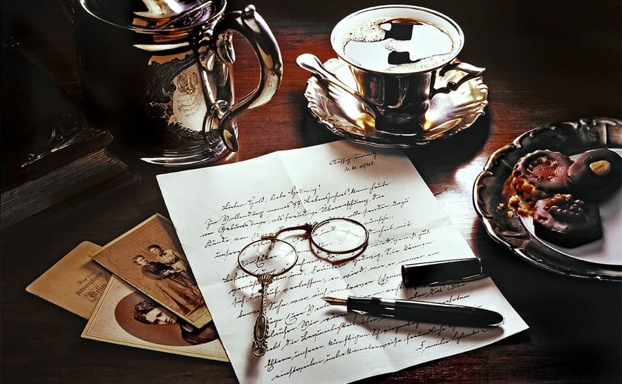 Old letters home with a monocle, fountain pen, tea, and some old photographs around it 