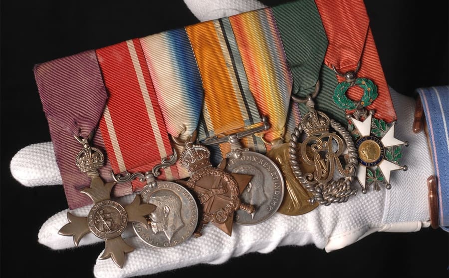 A person wearing a white glove holding a bunch of medals 