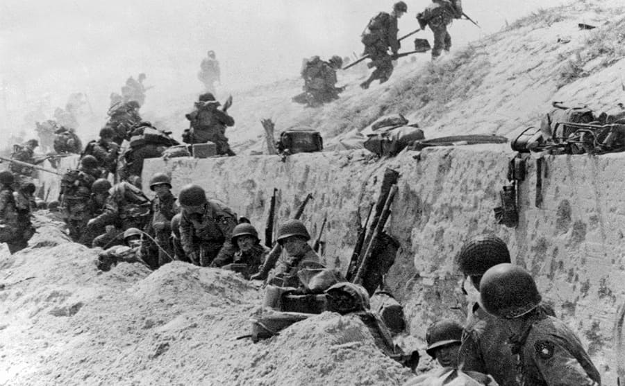 American troops sitting behind a wall while some climb up 