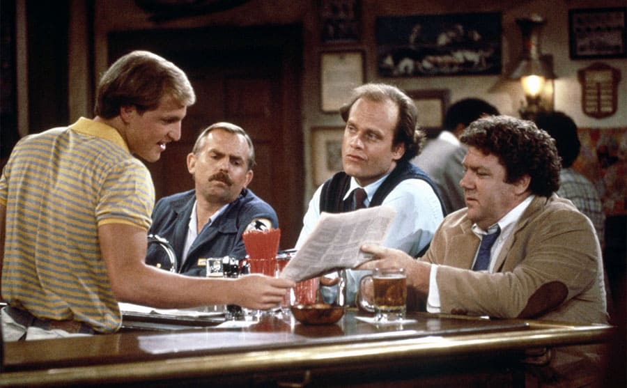 Woody Harrelson, John Ratzenberger, Kelsey Grammer, and George Wendt sitting at the bar in a scene from Cheers