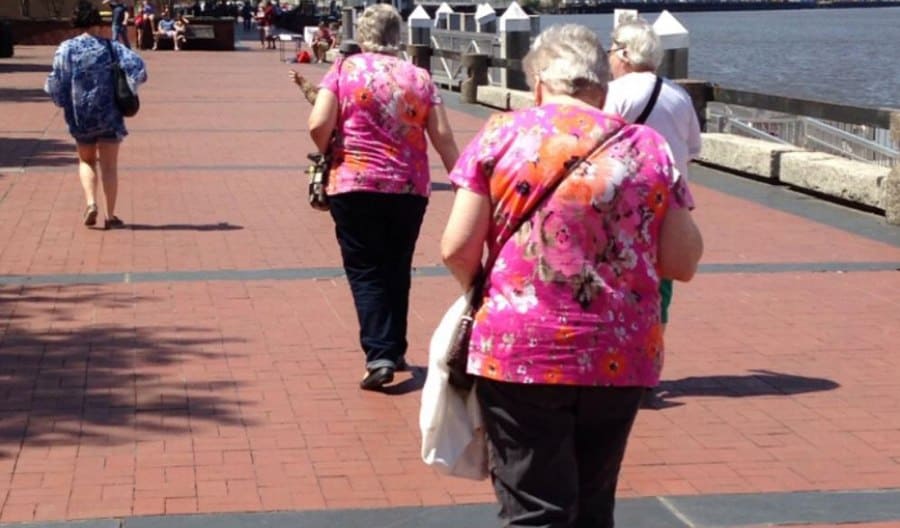 Two women with grey hair walking down a pier with matching pink floral shirts on 
