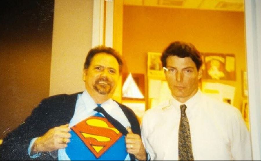 Christopher Reeves posing with a man holding his shirt open, exposing a Superman logo 