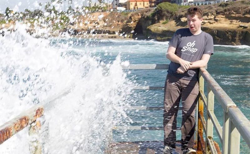 A kid about to get hit with splashed up water while wearing a shirt that says ‘oh snap!’