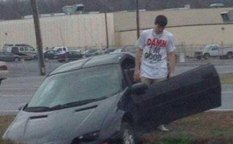 A car in a ditch with a guy getting out of the driver’s seat wearing a shirt that says Damn I’m Good 