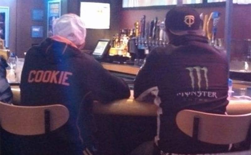 Two men at a bar, one wearing a sweater that says cookie and the other wearing one that says Monster 