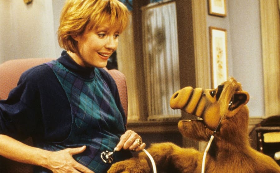 Anne Schedeen with ALF listening to her baby bump using a stethoscope 