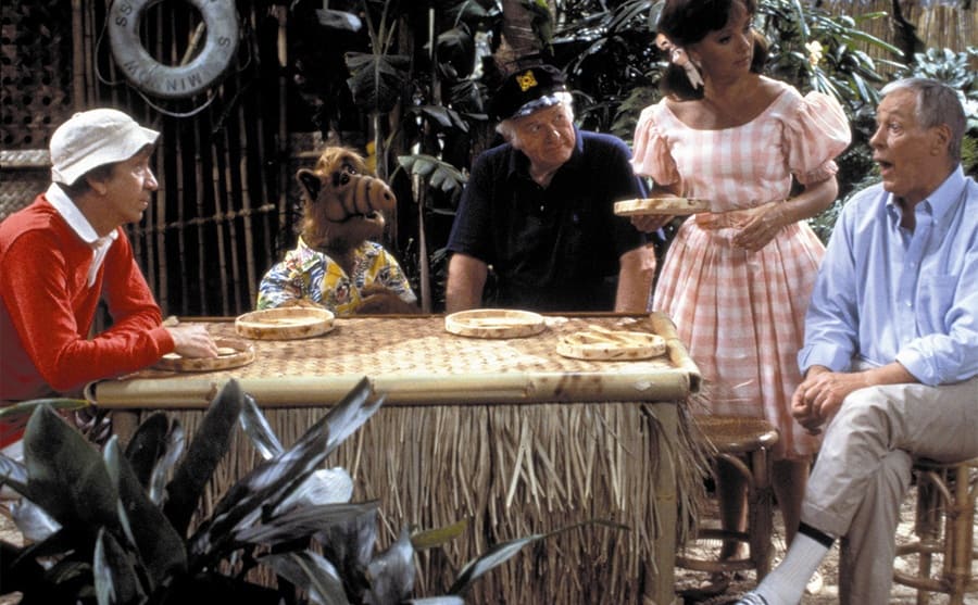 ALF sitting around a table with the cast of Gilligan’s Island 