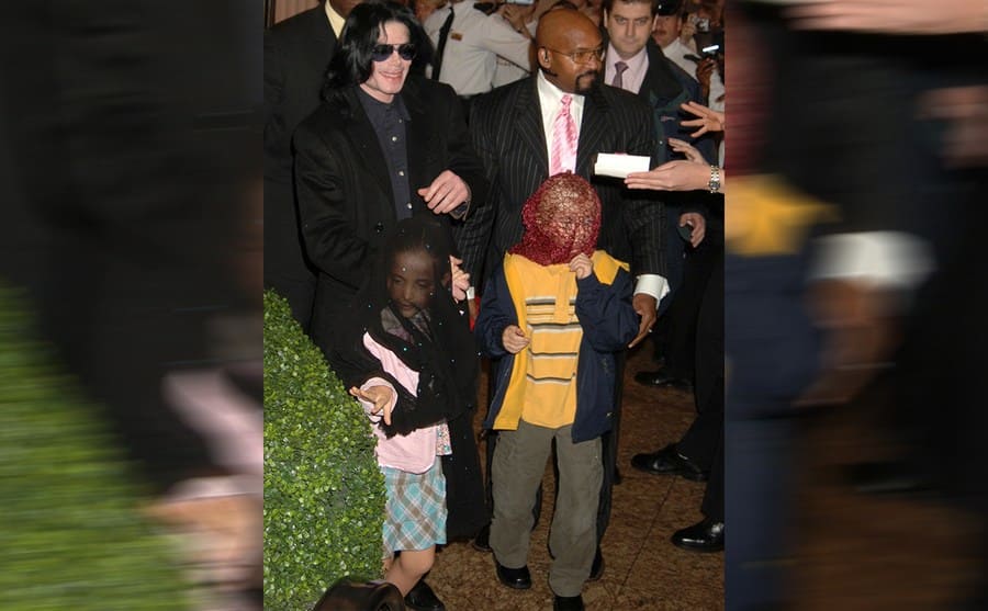 Michael Jackson surrounded by paparazzi with Paris and Prince Michael Jr wearing masks 