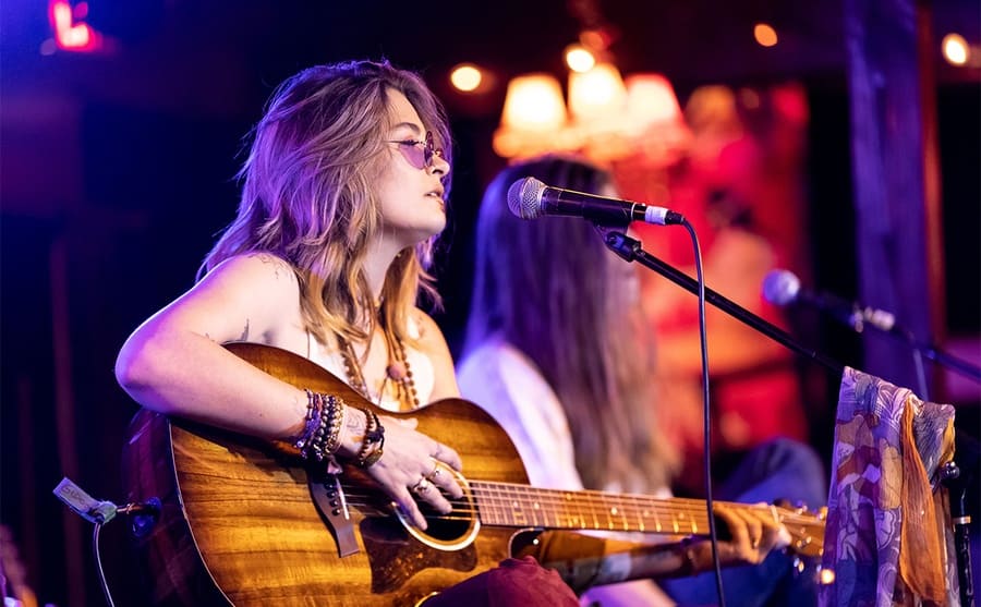 Paris Jackson performing on stage with an acoustic guitar 