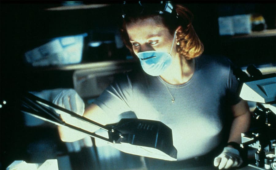 Gillian Anderson wearing a medical mask examines test tubes
