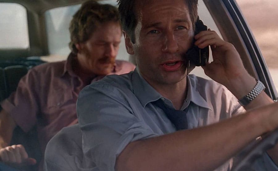 David Duchovny driving a car and Bryan Cranston sleeping in the back sit