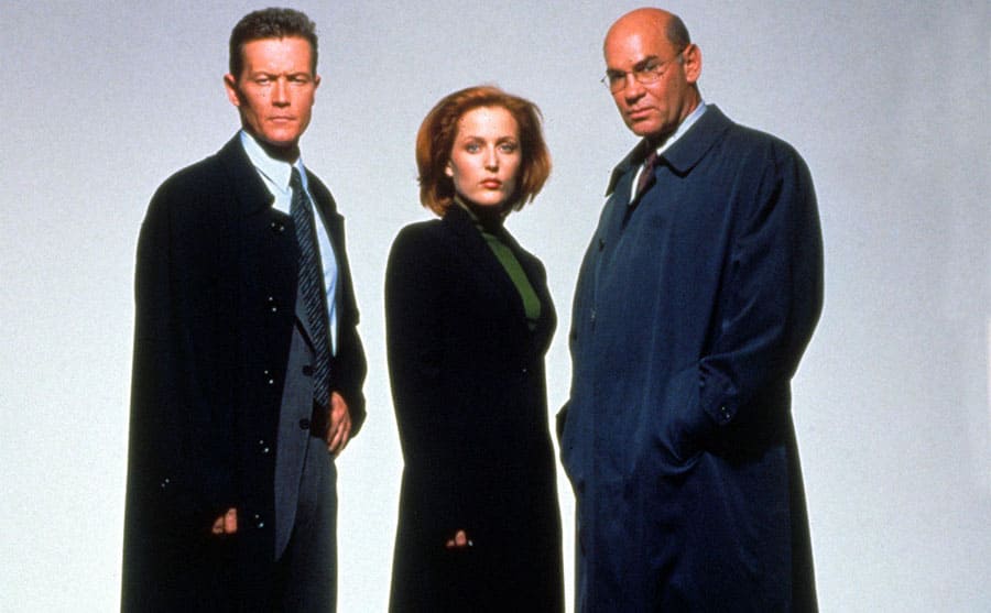 Robert Patrick, Gillian Anderson, and Mitch Pileggi standing together wearing long coats