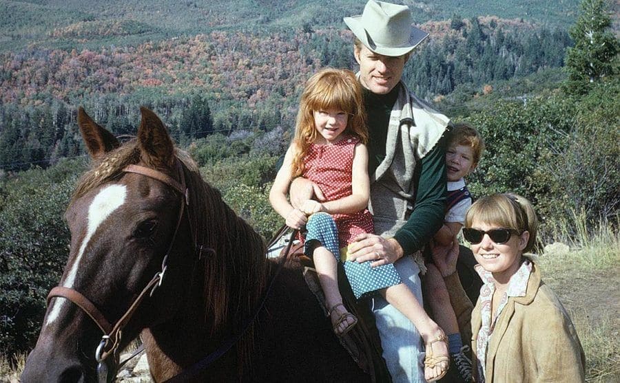 Robert Redford and his family posing on a horse with a mountain landscape in the background 