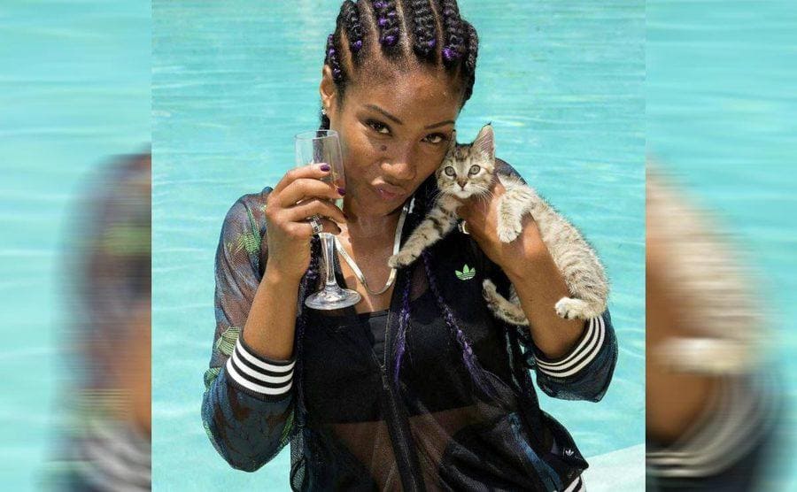 Tiffany Haddish holding a glass of champagne and the kitten that she adopted at the side of the pool 