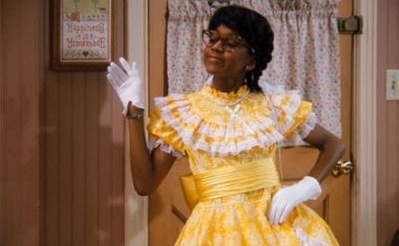 Steve Urkel dressed as Myrtle Urkel waving as he comes in the kitchen door in a scene from Family Matters