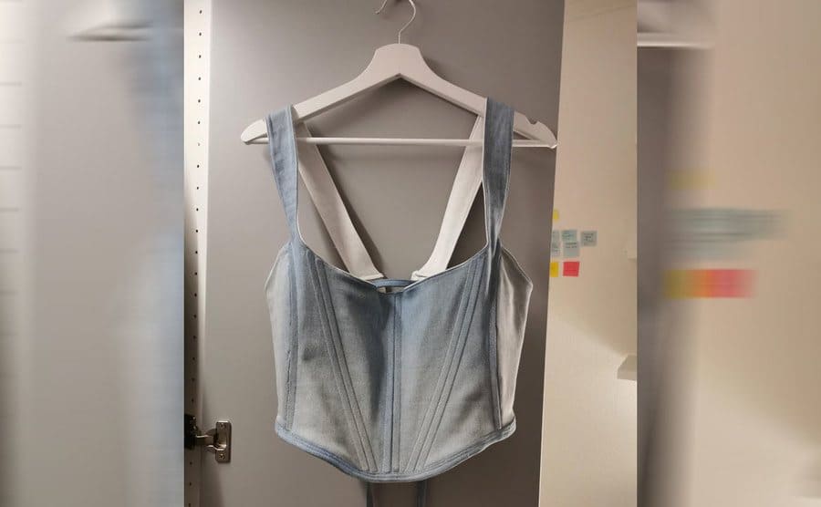 The jean corset with inch thick straps hanging from a hanger 