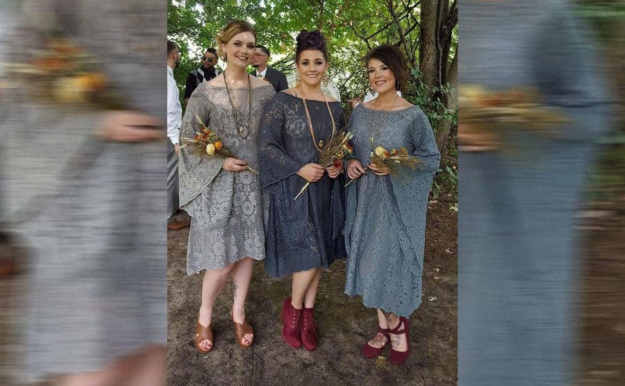 Three women wearing lacy and flowing short dresses made out of lace tablecloths in three different shades of grey 