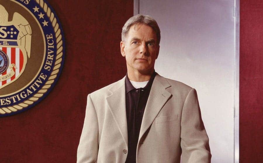 Mark Harmon as Special Agent Jethro Gibbs in a beige suit standing in a US government building 