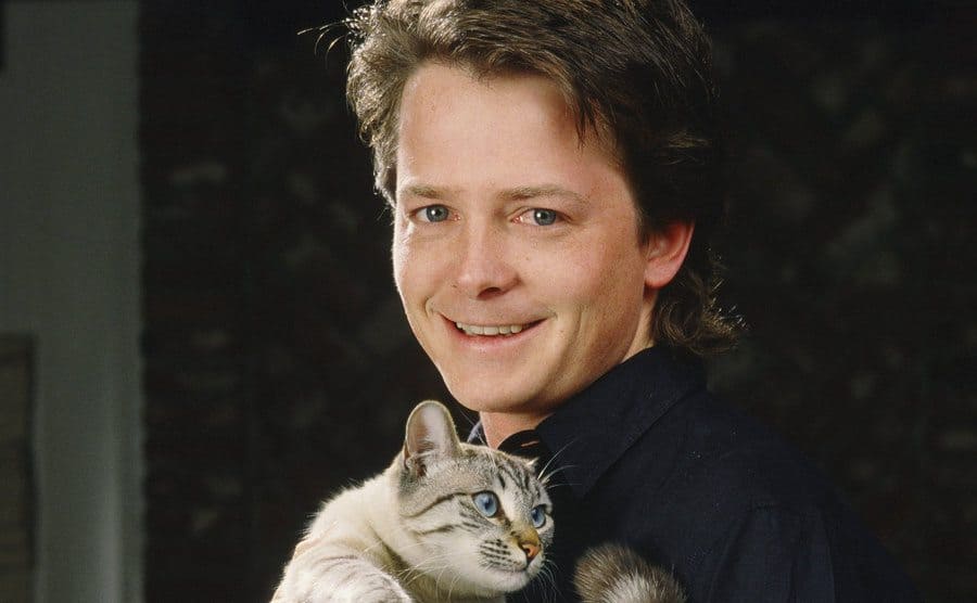 Michael J Fox posing with a cat during a photoshoot for Family Ties