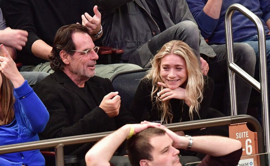 Ashley and Richard laughing together at a basketball game in the stands 