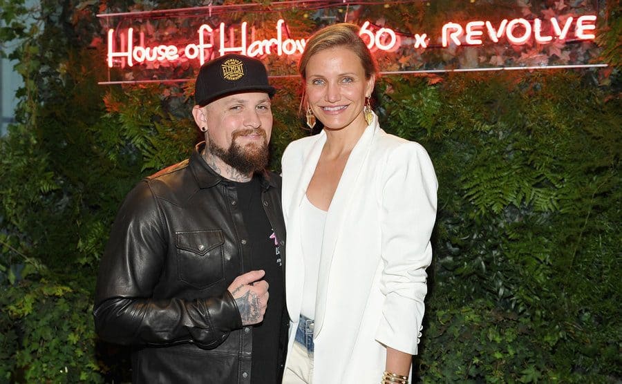 Benji Madden and Cameron Diaz at an event standing in front of leafy bushes 