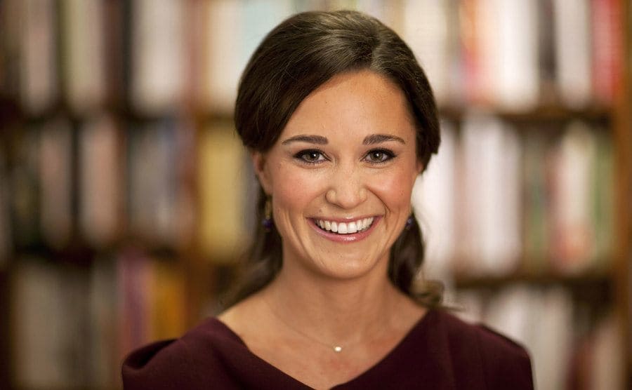 Pippa Middleton posing in front of a blurred out bookshelf at a library 
