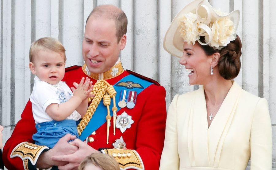 Prince William holding Prince Louis next to Catherine, both of them paying attention to Prince Louis 