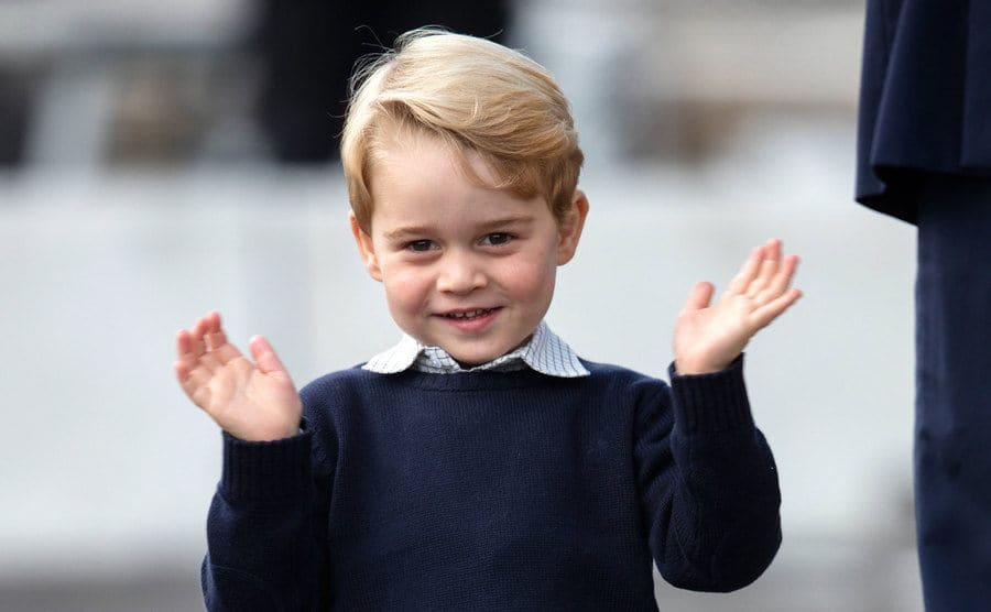 Prince George waving with both hands towards the direction of the camera 