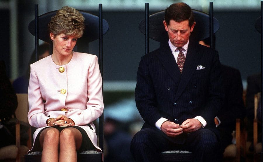 Princess Diana looking upset sitting next to Prince Charles who is looking downwards playing with his fingers 
