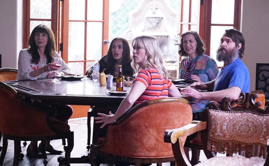 Will Forte sitting at the head of a dinner table with Kristen Schaal, January Jones, Cleopatra Coleman, and Mary Steenburgen sitting around him. Everyone is looking behind the view of the camera in shock 
