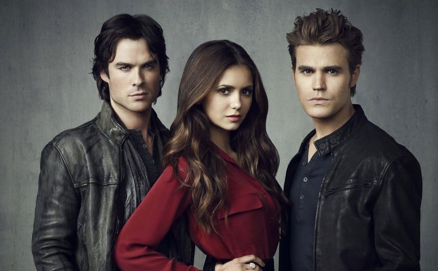 Ian Somerhalder, Paul Wesley, and Nina Dobrev starring into the distance in a coffin warehouse 