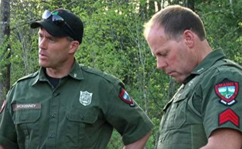 Two park rangers in uniform looking serious in the woods