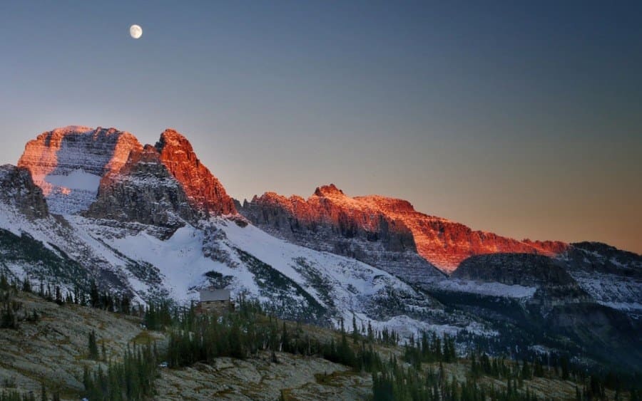 Granite Park Chalet beneath Snow Capped Mountains and Rising Moon at Sunset, Glacier National Park, Montana, USA.