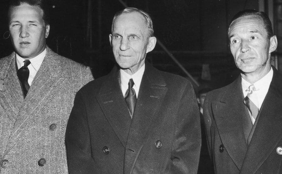 Henry Ford II, Henry Ford, and Edsel Bryant Ford posing together in trench coats 