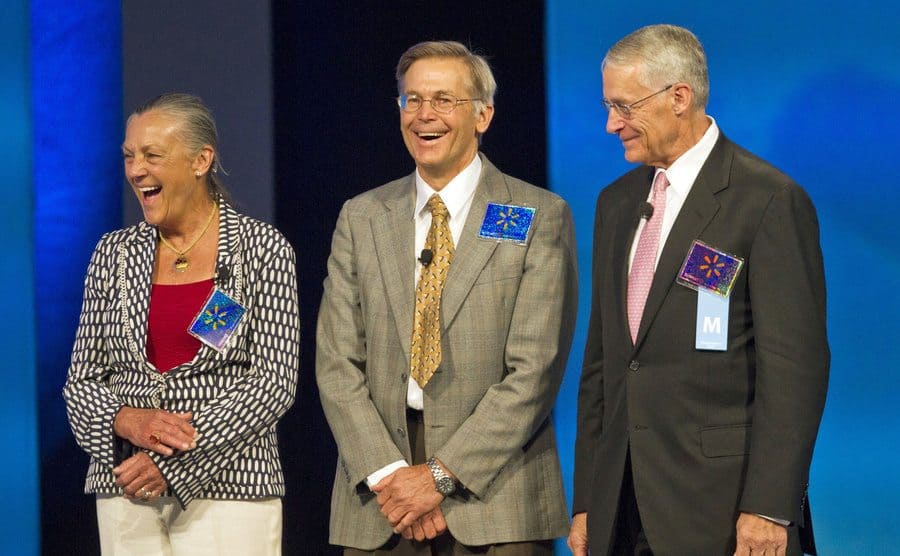 Alice, Jim, and Rob Walton on stage with WalMart stickers on their jackets