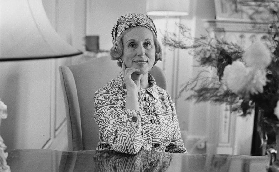 Estee Lauder posing on a desk leaning gracefully on her hand 