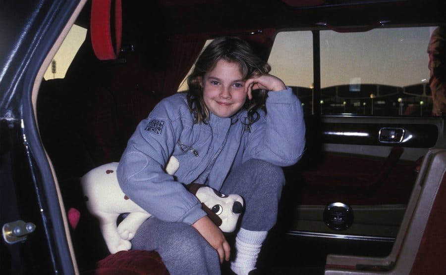 Drew Barrymore sitting in the back of a car with a stuffed animal in 1985