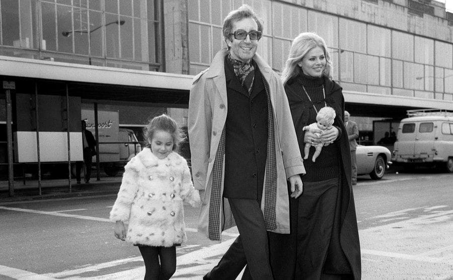 Peter Sellers with his daughter and wife, carrying her daughter's doll at the airport 