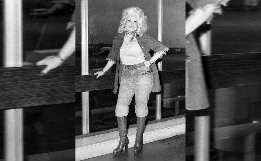 Dolly Parton at the airport leaning against a railing next to a large window 