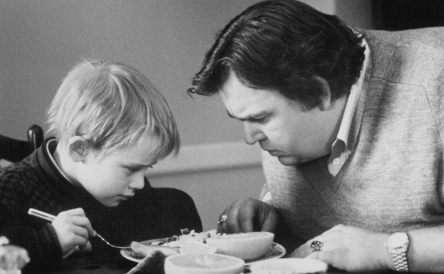 Macaulay Culkin looking at a plate of food with John Candy in a scene from Uncle Buck 