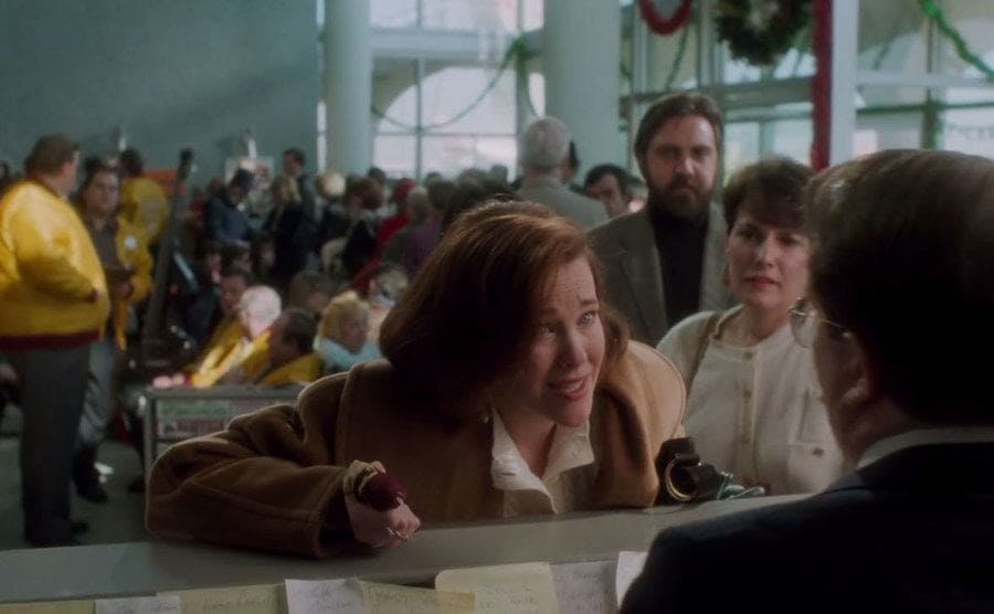 Kevin’s mom at the airport counter with the man standing behind them with a beard 