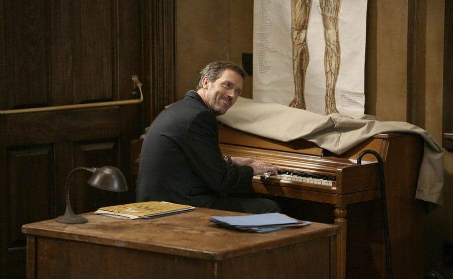 House is playing an old dusty piano. 