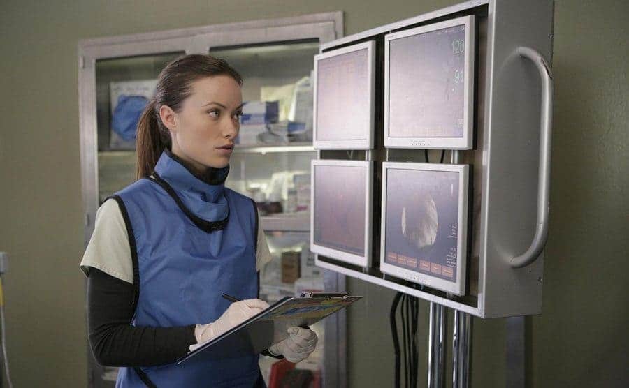 Olivia Wilde is reading x-rays while writing on a clipboard. 