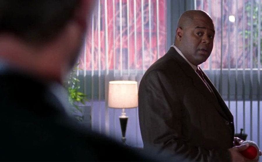 Chi McBride as Edward Volger standing in an office.