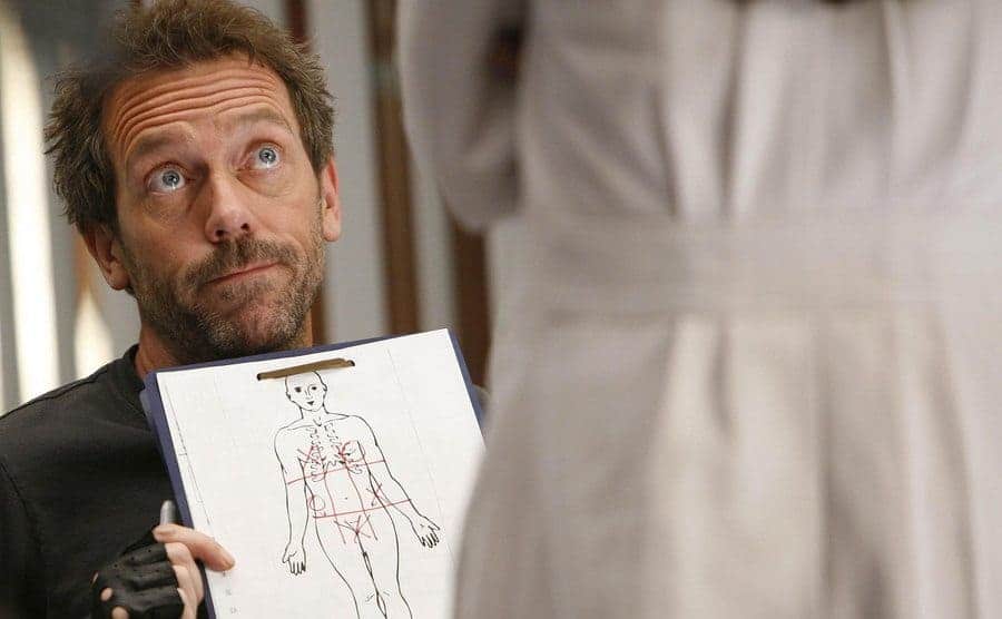 House is showing another doctor a drawn chart of the human body. 