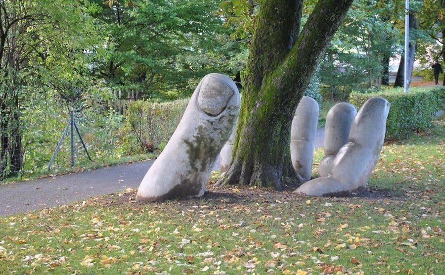 A sculpture of a hand sticking out from underneath a tree trunk 
