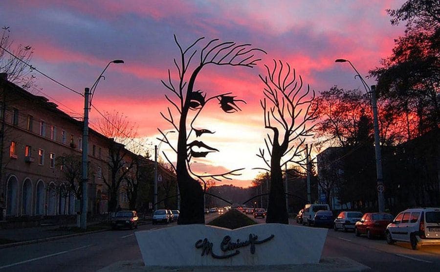 A sculpture in the outline of a man's head with a pink and purple sunset behind it 