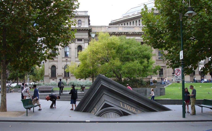 The statue of a tip of a library building sticking out of the ground 