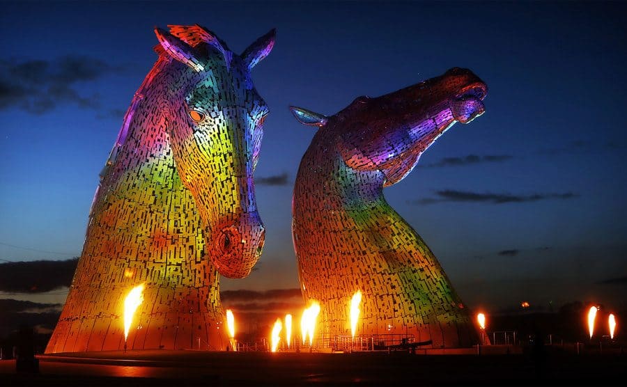 The Kelpies lit up with colors and flames around them 