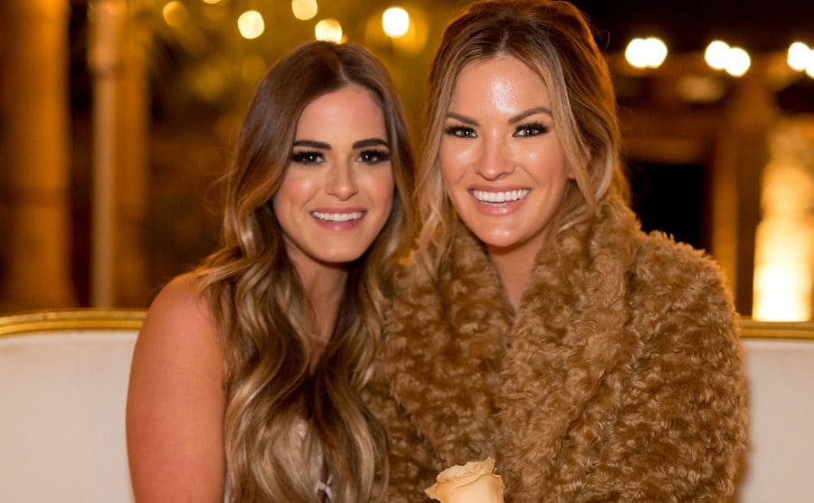 JoJo Fletcher and Becca Tilley of the Bachelor sitting outside with white roses 